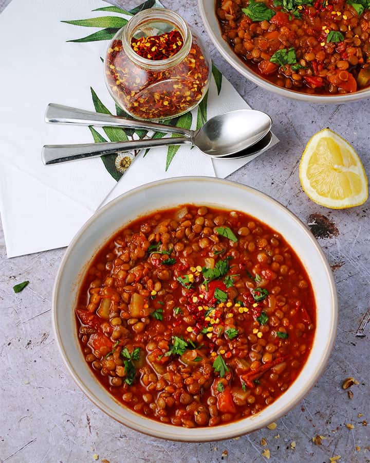 Overhead shot of lentil tomato soup bowls with chopped parsley and red chili flakes