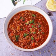 Lentil tomato soup in bowl garnished with chopped parsley and red chili flakes