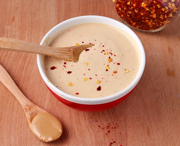 dressing made with tahini and orange juice in small red bowl with small wooden spoon.