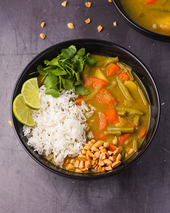 veggie massaman curry with rice, chopped peanuts and cilantro in black bowl.
