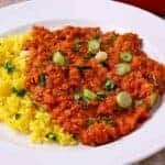 cooked red lentils and tomatoes on white plate with yellow rice and chopped parsley and scallions