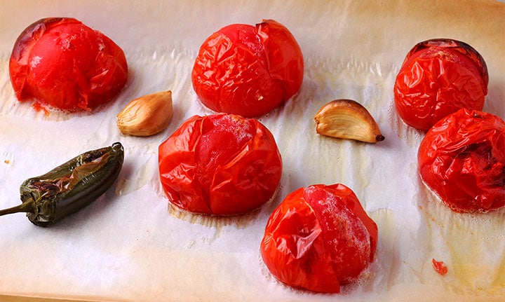 Tomatoes, jalapeno and garlic are roasted on baking tray with parchment paper.