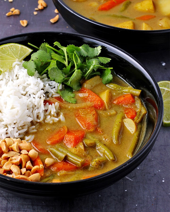 veggie massaman curry with rice, chopped peanuts and cilantro in black bowl.