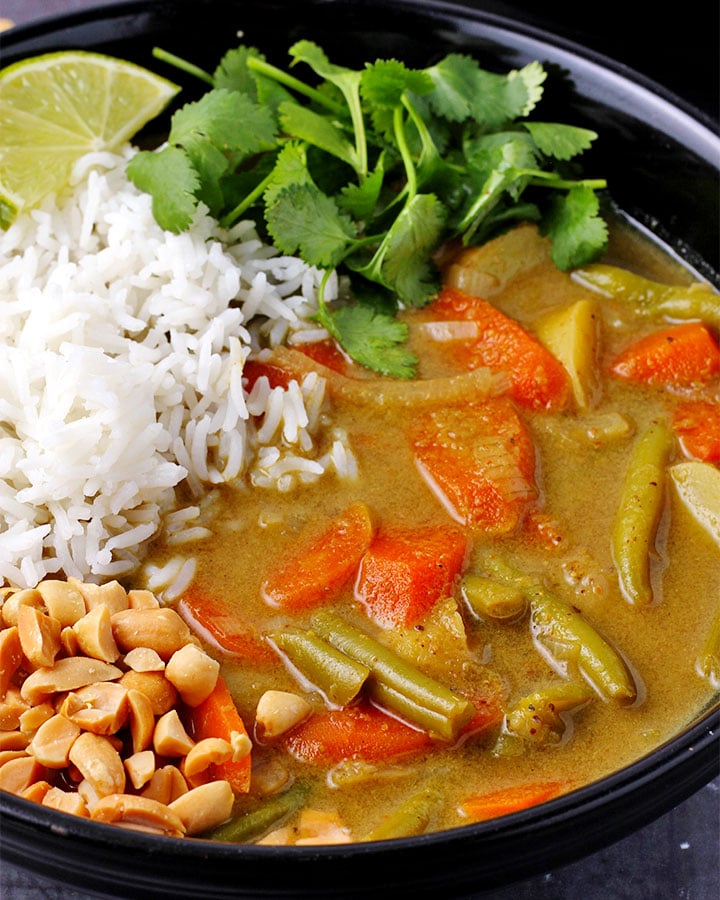 Close up of veggie massaman curry with rice, chopped peanuts and cilantro in black bowl.