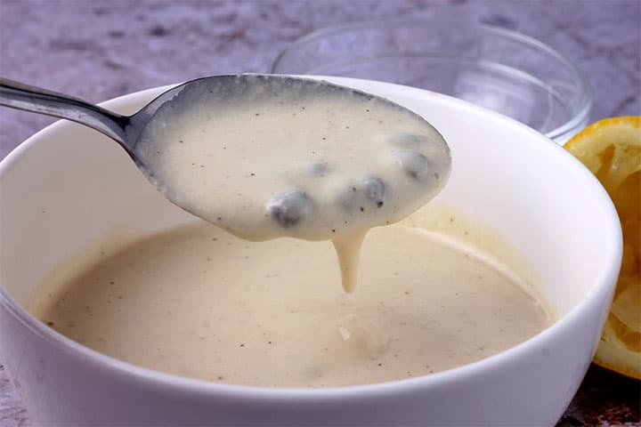 white bowl with Caesar dressing with capers and spoonful of dressing