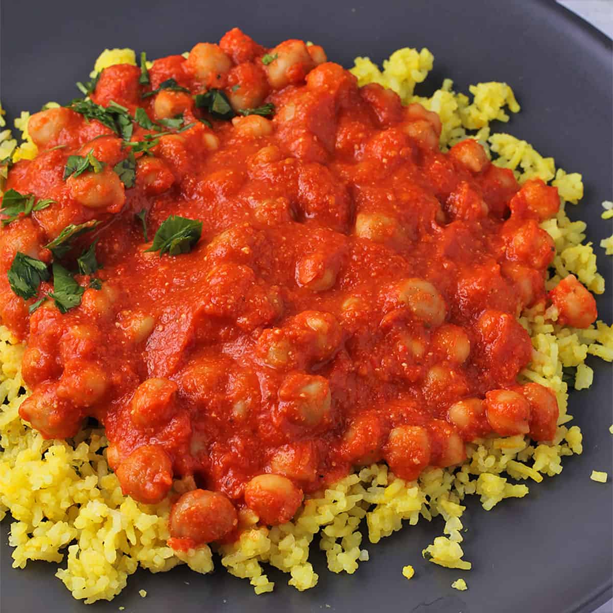 Chickpeas in red pepper sauce romesco sauce over yellow rice with chopped parsley on black plate