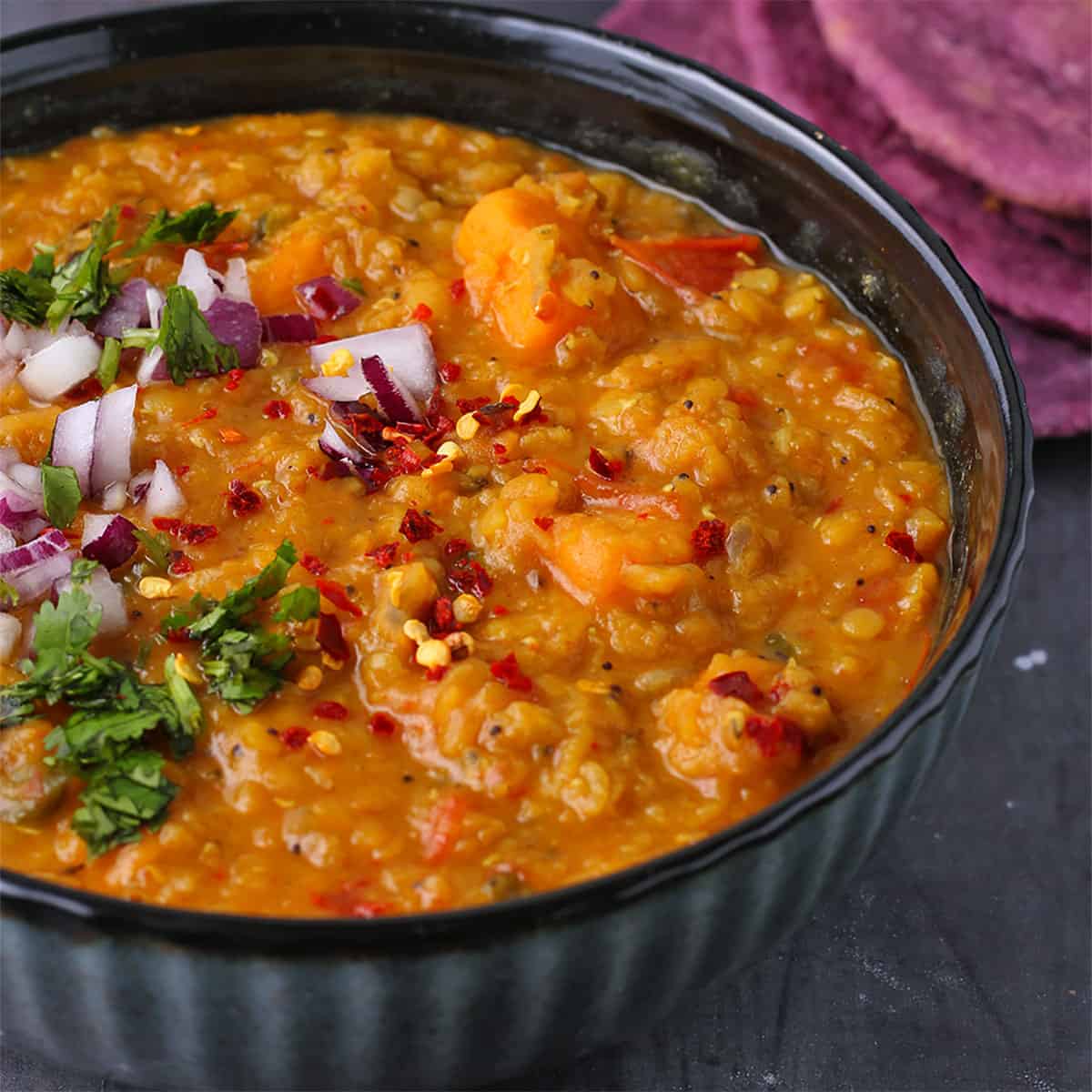 sweet potato dahl with red lentils in black bowl with coriander, diced red onions and red chili on top.