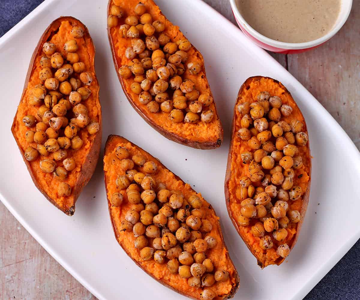 baked sweet potato halves on white plate with chickpeas on top