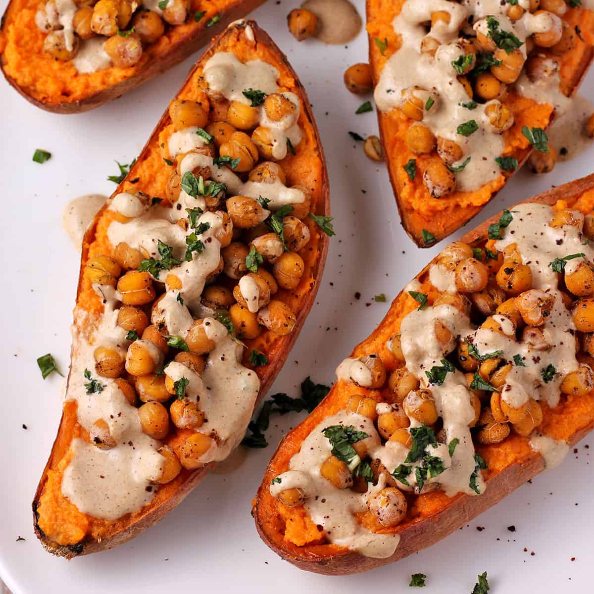 Baked sweet potatoes are cut in half and topped with baked chickpeas, dressing and chopped green mint.