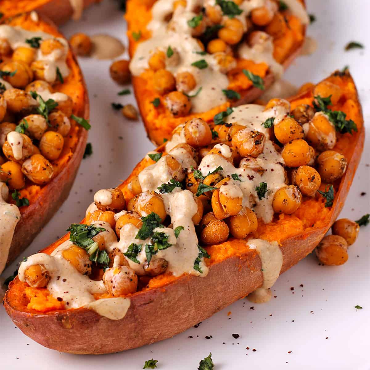 Baked sweet potato halves with chickpeas, dressing and chopped mint on top