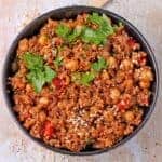 cooked quinoa with chickpeas with red pepper, sesame seeds, and chopped parsley in black bowl.