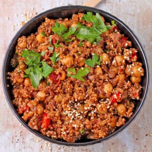cooked quinoa with chickpeas with red pepper, sesame seeds, and chopped parsley in black bowl.