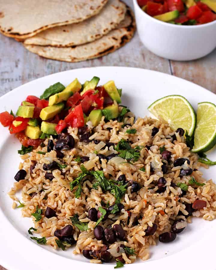 white plate with cooked rice and black beans with chopped cilantro and diced avocado and tomatoes