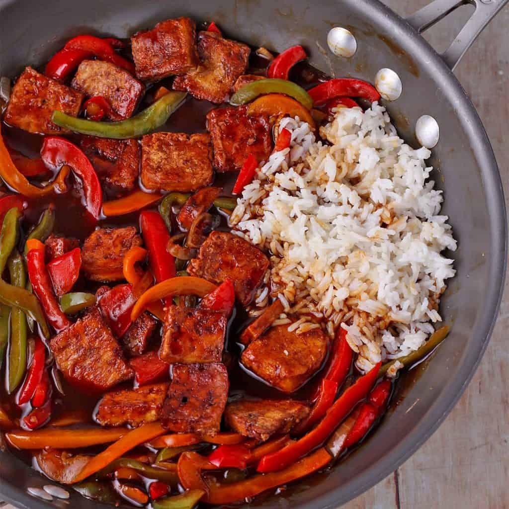 sweet and sour tofu with sliced peppers and scoop of white rice in wok.