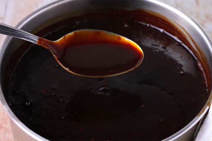 spoonful of sweet and sour sauce is held over pan