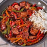 sweet and sour tofu with pepper and onion slices and white rice in wok