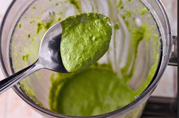 Cilantro lime dressing in spoon held over blender.