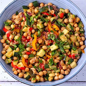 Blue serving bowls with chickpea stew with diced zucchini, red and yellow peppers, red onions and chopped parsley.