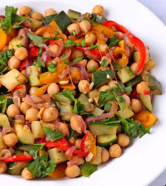Colorful chickpea stew with diced zucchini, red and yellow peppers, red onions, chickpeas and chopped parsley in white bowl.