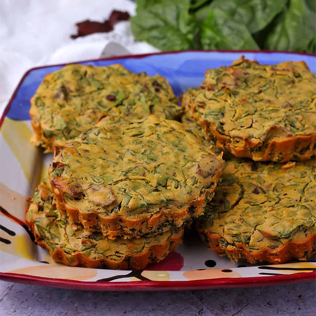 vegan mini quiches with spinach and bacon are stacked on a plate