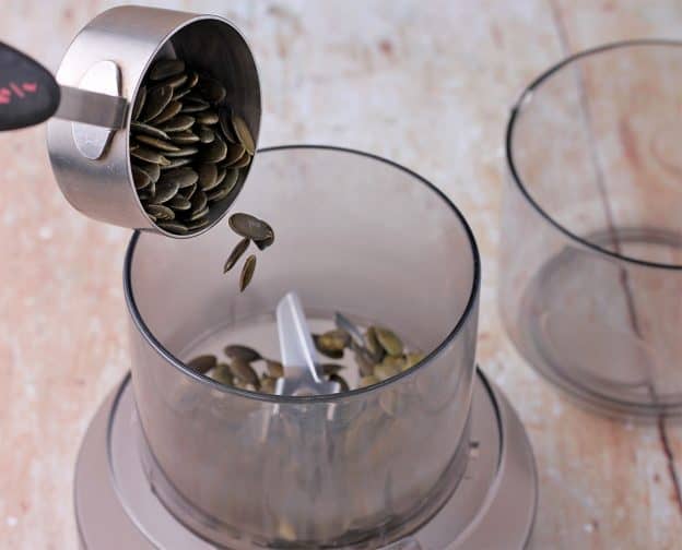 Pepitas are poured from a cup into a spice grinder
