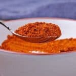 A spoonful of red Ethiopian berbere spice mix is held over white dish of blend