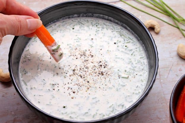 a carrot is dipped into plant-based ranch dressing with ground pepper