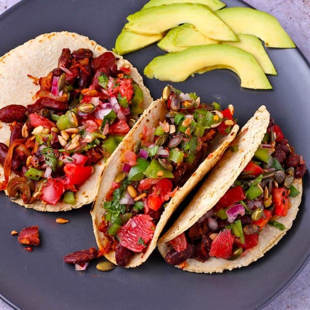 3 tacos with kidney beans, grapefruit, cilantro, and pepitas on black plate