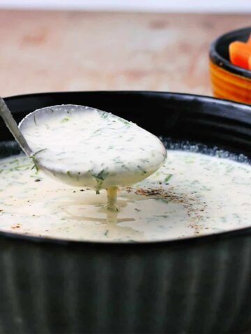 plant-based cashew ranch dressing in a blue bowl with a ladle of dressing.
