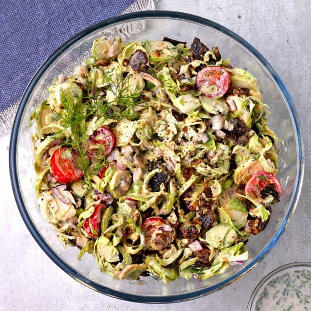 Shaved Brussels sprouts salad with bacon, red onion, tomatoes, and ranch dressing in glass bowl