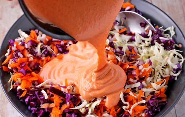Fiery sriracha-tahini dressing is added to shredded green and purple cabbage, and grated carrots.