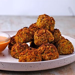 A stack of veggie balls on white plate with small dish of dressing.