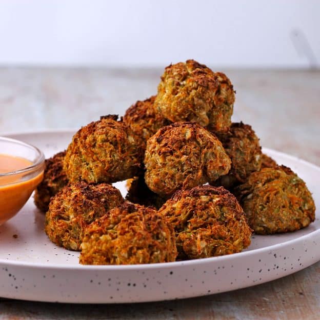 a plate of veggie balls are stacked up on a white plate with small dish of dressing.