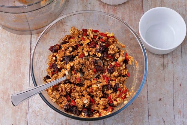 Glass bowl with oats, dried cranberries, Goji beans, and walnuts mixed with blended almond paste, dates, and orange juice