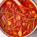 Pot with stew of green beans, potatoes, kidney beans, and tomatoes with wooden spoon