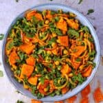 A blue salad bowl is filled with roasted sweet potatoes, chopped kale, turmeric chickpeas, and red onions.