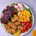 A salad of savory baked tofu, orange and beetroot, with sliced tomatoes, radishes, and arugula.