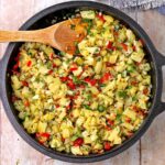 A black cast iron skillet is filled with pineapple chutney with cumin seeds, red chilies, cilantro, onion, ginger, and diced pineapple.