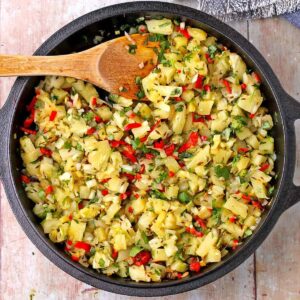 A black cast iron skillet is filled with pineapple chutney with cumin seeds, red chilies, cilantro, onion, ginger, and diced pineapple.