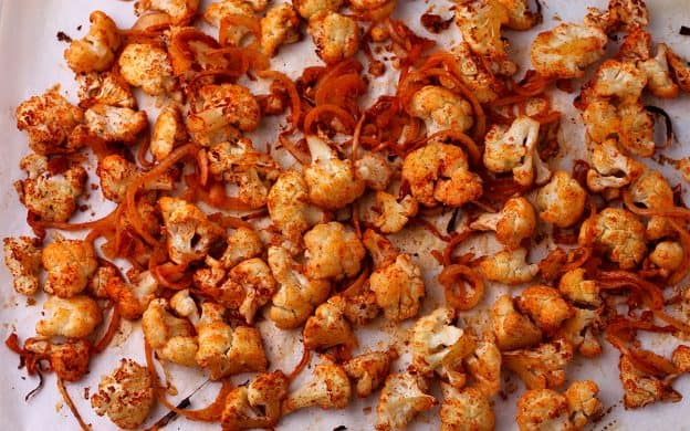 A baking tray with cauliflower and sliced onions covered in taco seasoning and roasted.