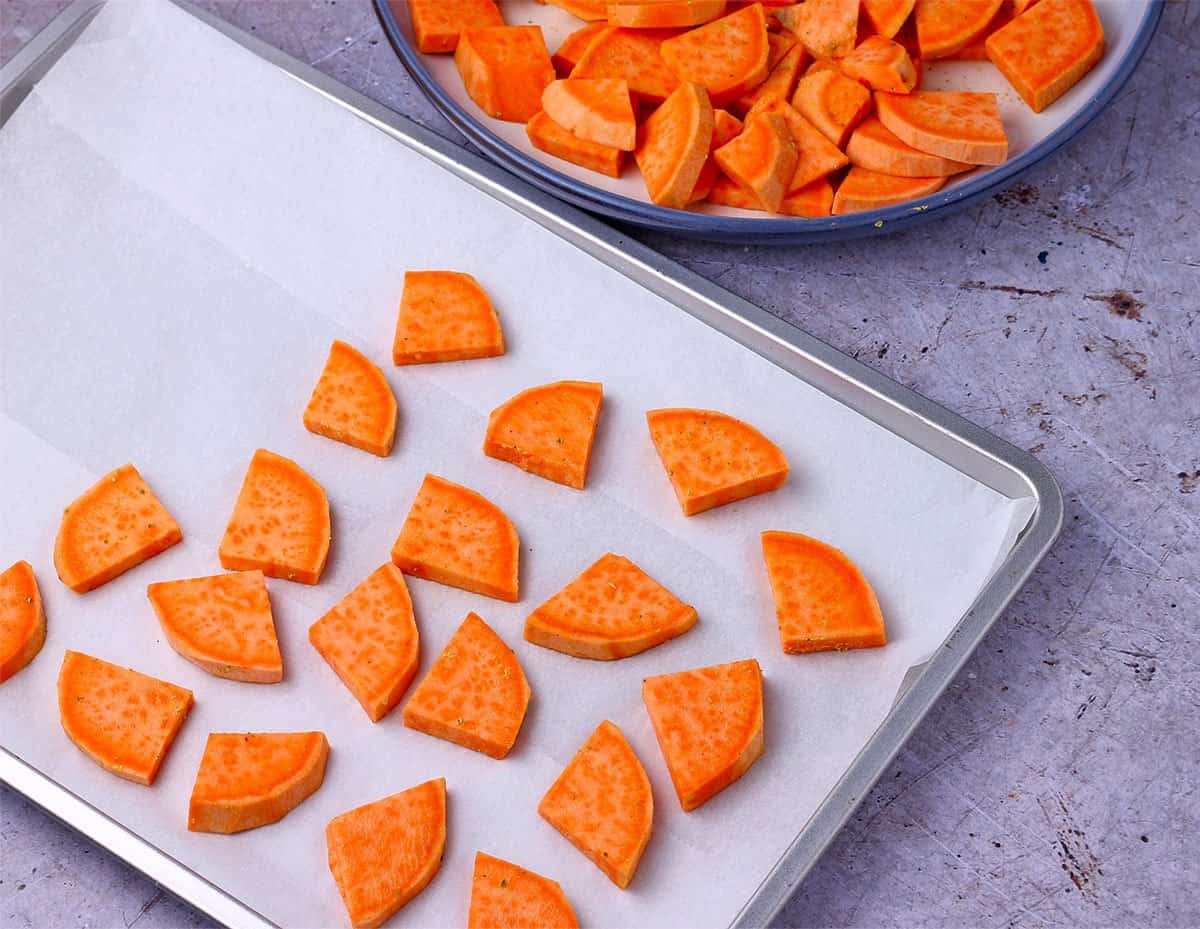 Sweet potato slices are laid on a baking tray lined with parchment paper.