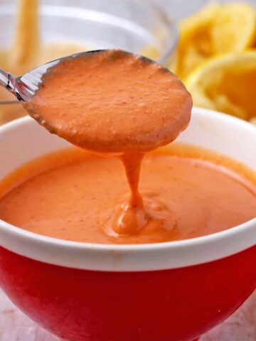 A spoonful of sriracha-tahini dressing is held over a red bowl.