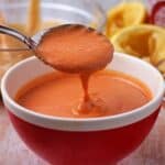 Fiery sriracha-tahini dressing in a red bowl with a spoonful held over the bowl.