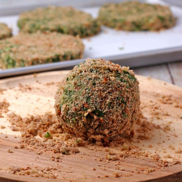 A spinach and potato ball is rolled in whole wheat bread crumbs.