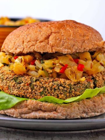 Spinach and potato patty in a bun with lettuce and pineapple chutney on black plate.