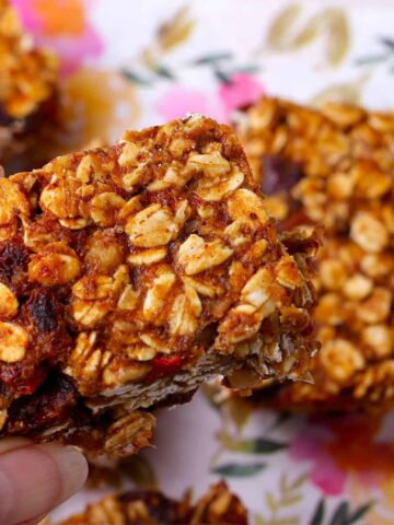 baked granola bar is held over a plate of granola bars