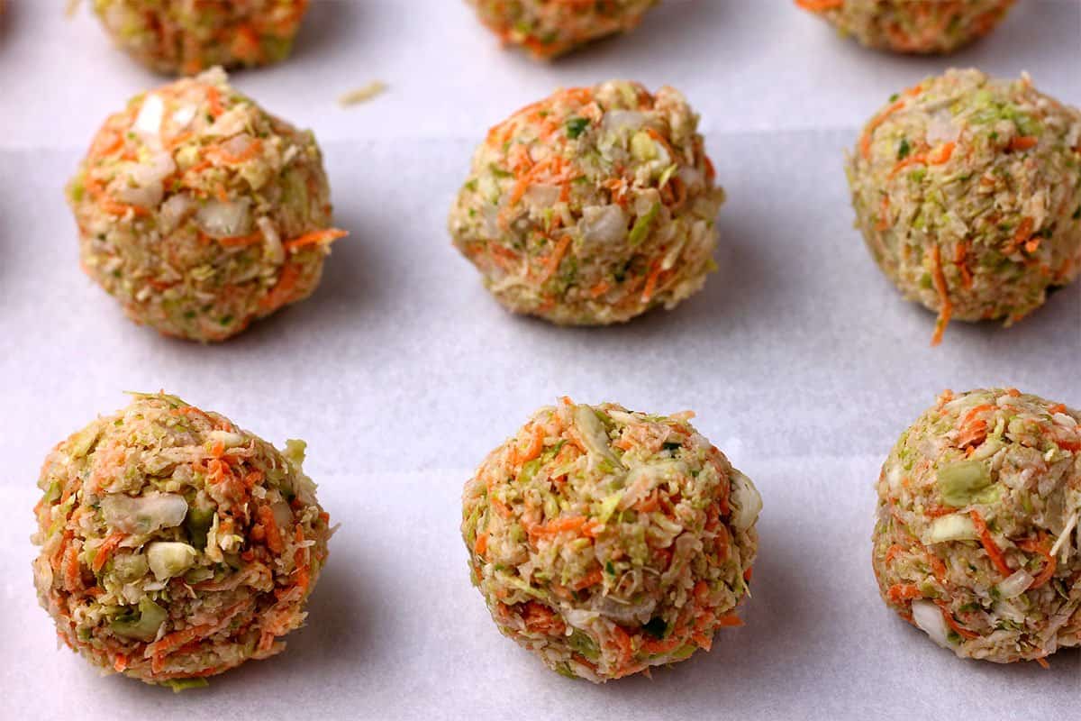 Unbaked veggie balls are placed on a tray with parchment paper.