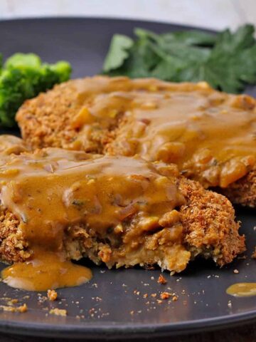 Chickpea cutlets topped with mustard sauce are placed on a black plate with steamed broccoli.