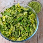 A bowl is filled with chopped romaine lettuce, sliced cucumber, snap peas, scallions, and healthy green goddess dressing.