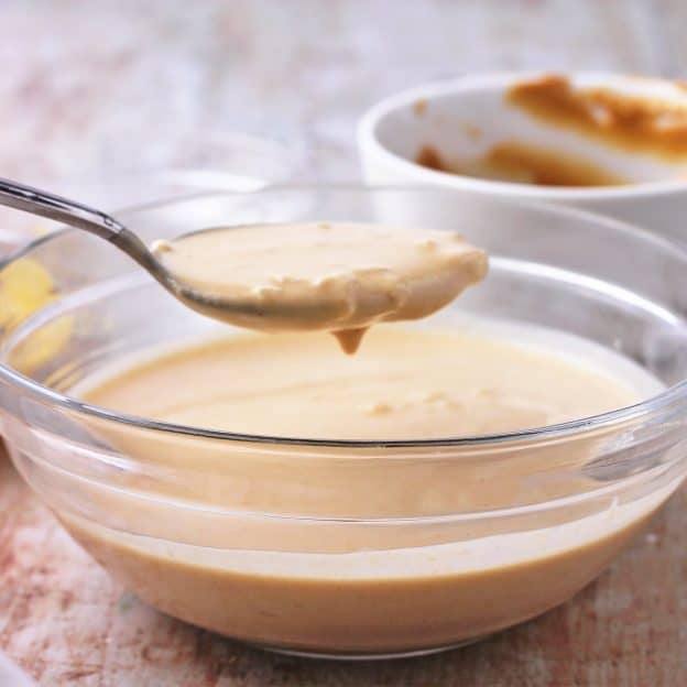 A spoonful of lemon tahini salad dressing is held over a bowl of dressing.